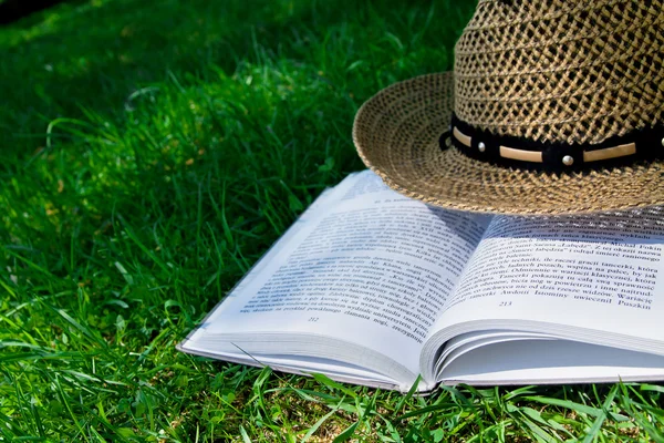 Book and straw hat on grass — Stock Photo, Image