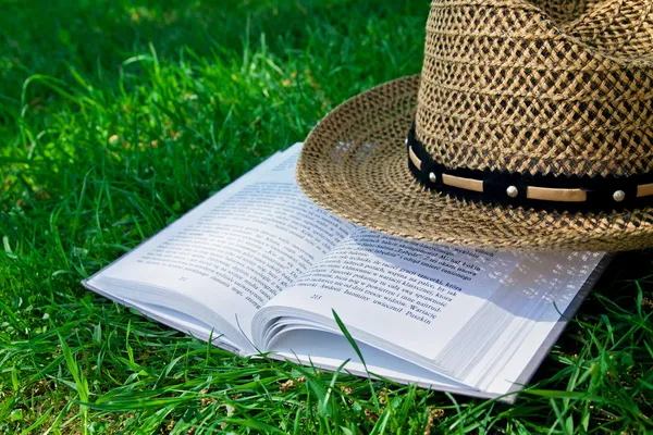 Kniha a sláma klobouk na trávě — Stock fotografie