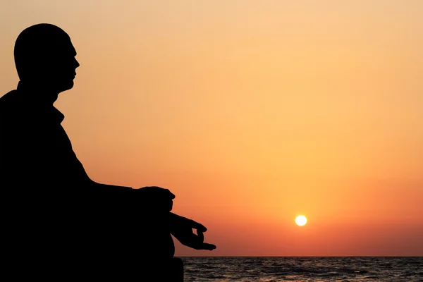 A young man sitting in lotus position and meditating on a beach — Stock Photo, Image