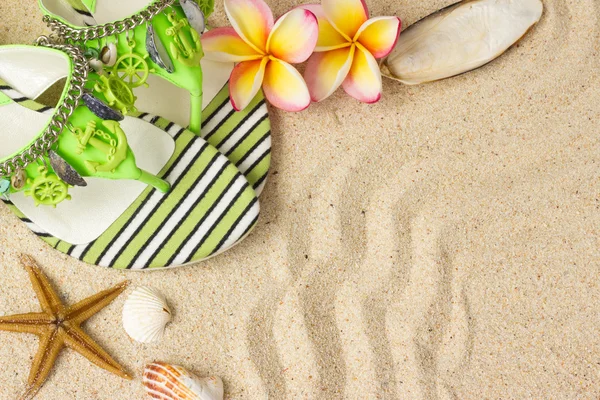 Sandalias verdes, conchas marinas, estrellas de mar y frangipani sobre arena —  Fotos de Stock