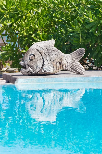 Swimming pool with wooden carved fish sculpture on the side — Stock Photo, Image