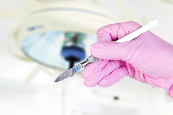 Скальпель в руке хирурга под лампой — стоковое фото