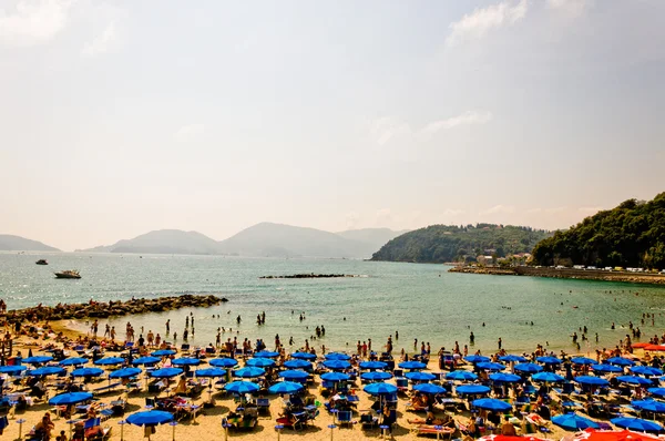 Přeplněné pláže Ligurského moře, lerici, Itálie s modrými deštníky — Stock fotografie