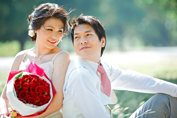 Portrait of bride and groom making eye contact with rose bouquet — Stock Photo, Image