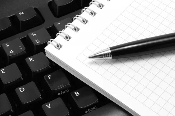 Bloco de notas com caneta em um teclado de computador preto — Fotografia de Stock