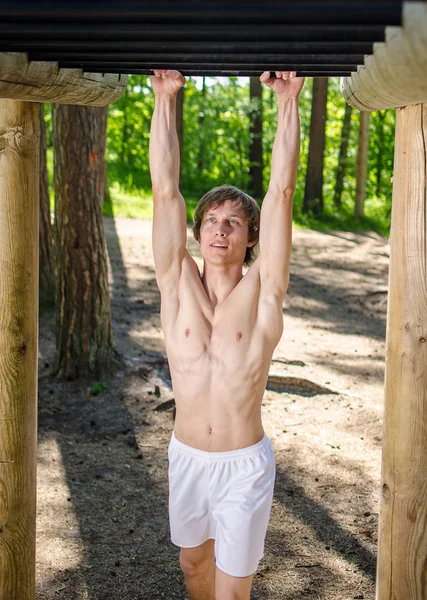 Atrakcyjny mężczyzna pull-up na pasku w lesie — Zdjęcie stockowe