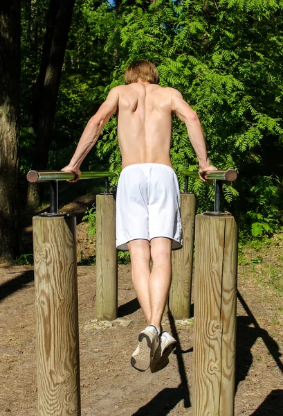 Człowiek pull-up na pasku w lesie. z tyłu. — Zdjęcie stockowe