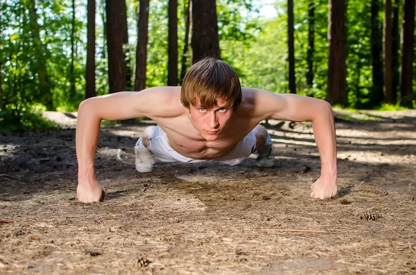 Attractive man doing a push up in forest — Stock Photo, Image