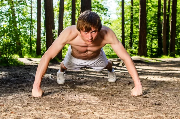 Atrakcyjny mężczyzna robi push up w lesie — Zdjęcie stockowe