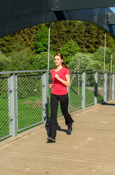Junge attraktive Frau joggt auf der Brücke — Stockfoto