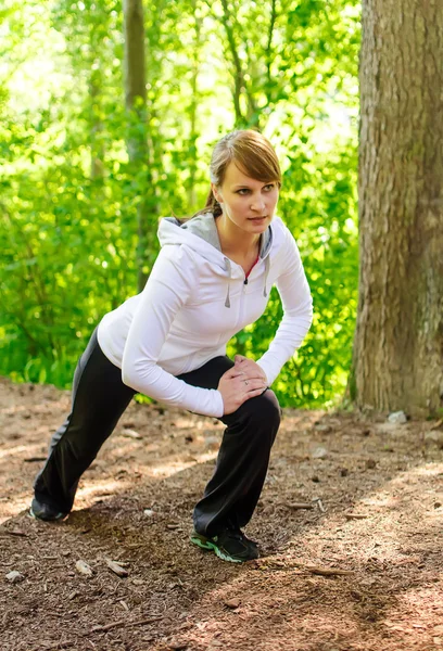 Attractive young woman stretching in forest — Stock Photo, Image
