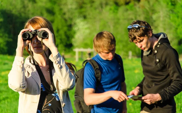 Three friends traveling. Girl looking through binoculars — Stock Photo, Image
