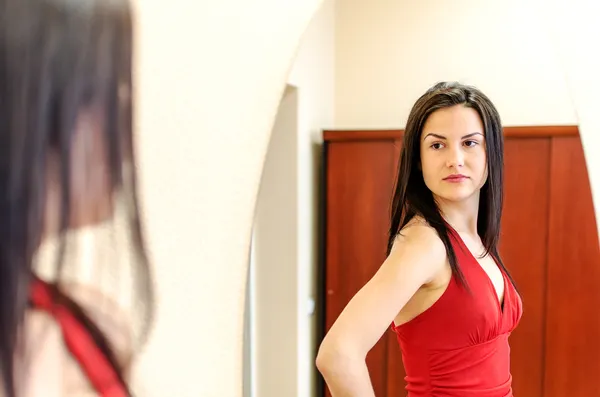 거울 앞에서 포즈를 취하는 빨간 드레스에 아름 다운 여자 — 스톡 사진