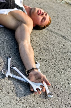 Tired mechanic laying on the road with stainless steel wrench in his hand clipart