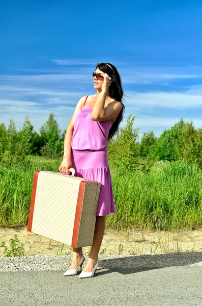 Una mujer en una carretera con una maleta está esperando un coche . — Foto de Stock