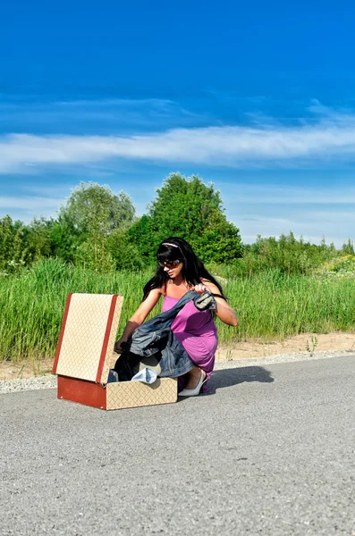 Vrouw op een weg krijgen kleren van koffer. — Stockfoto