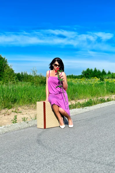 Mujer con rosa sentada en la maleta en el camino —  Fotos de Stock