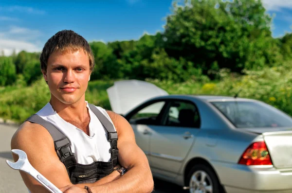 Knappe mechanic op een weg in de buurt van de gebroken auto. — Stockfoto