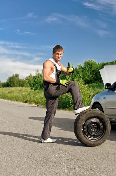 Mecánico guapo con un neumático en una carretera — Foto de Stock