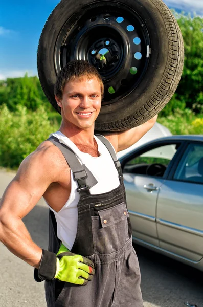 Retrato de un mecánico guapo sosteniendo un neumático en el hombro — Foto de Stock