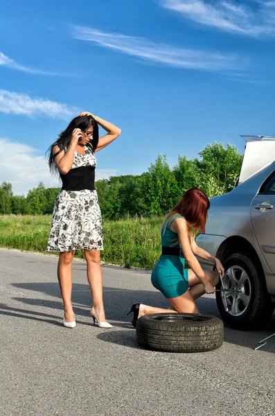 Duas mulheres estão a mudar um pneu numa estrada. — Fotografia de Stock
