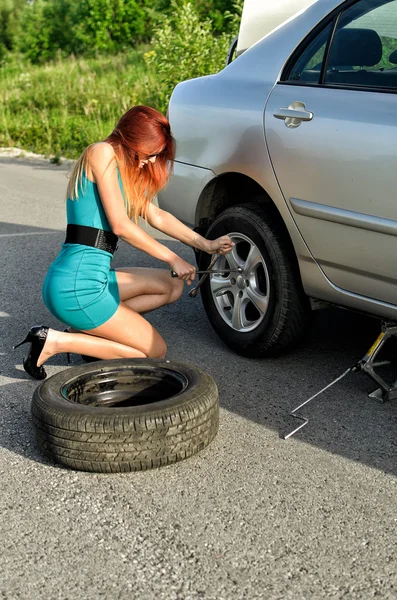 Chica bonita está tratando de cambiar un neumático en un camino —  Fotos de Stock