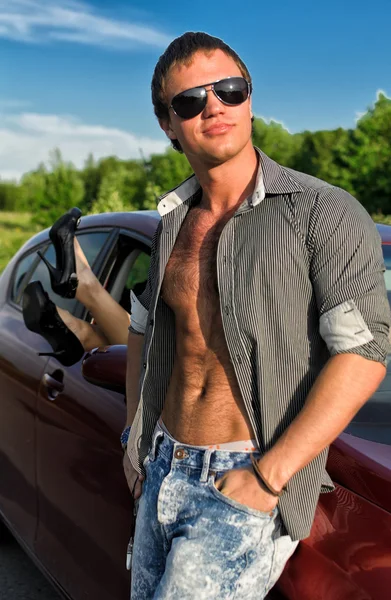 Sexy man posing near the car with woman legs stick out the window — Stock Photo, Image