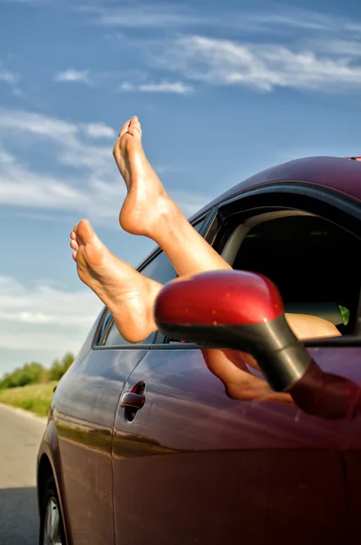 De benen van de vrouw uit het raam van de auto. concept van zorgeloos grappige reis. — Stockfoto