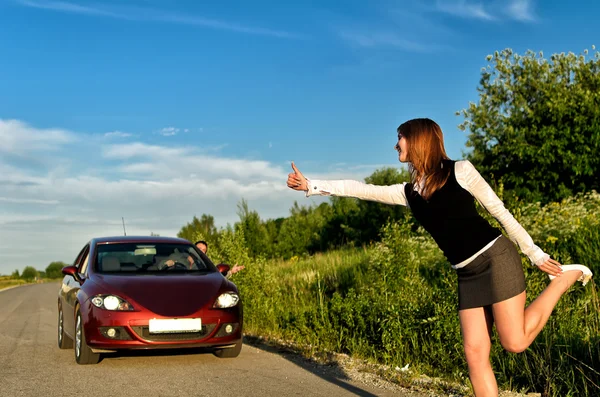 Young pretty girl hitchhiking a red car — Stock Photo, Image