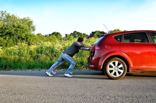 Man and woman pushing a broken car — Stock Photo, Image