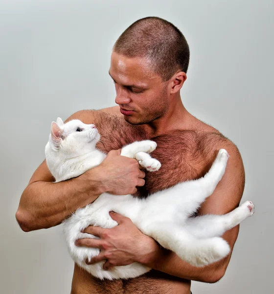 М'язистий чоловік тримає білого кота. На сірому фоні . — стокове фото