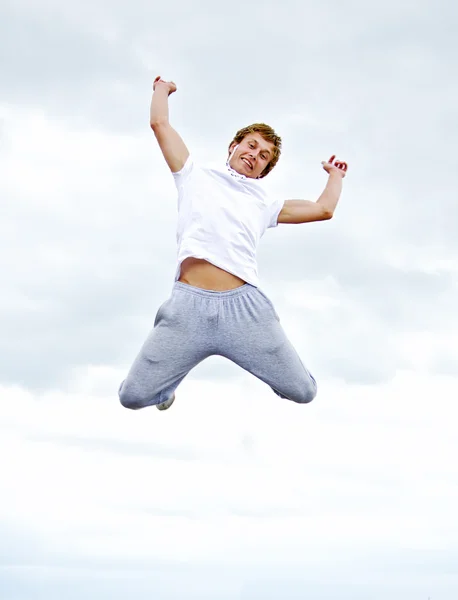 一个快乐的年轻人跳跃在空气反对天空的肖像. — 图库照片