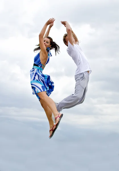 Porträtt av en lycklig ung par hoppar i luften mot himlen. — Stock fotografie