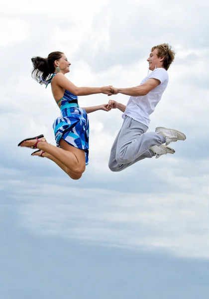 Porträtt av en lycklig ung par hoppar i luften mot himlen. — Stockfoto