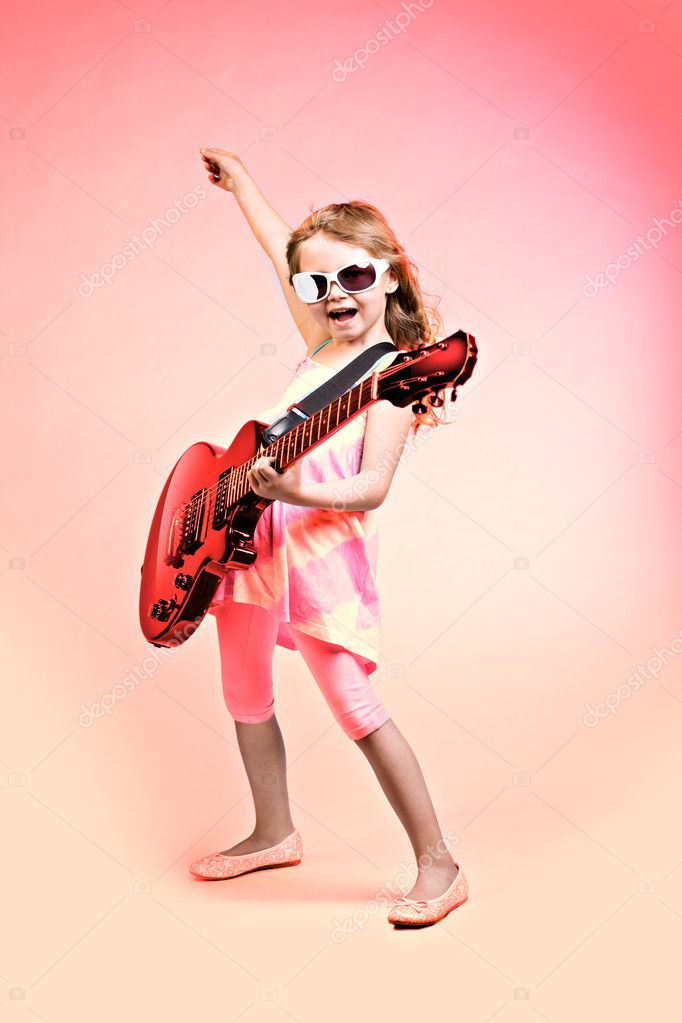 Cute little girl in summer clothing playing ukulele over pink