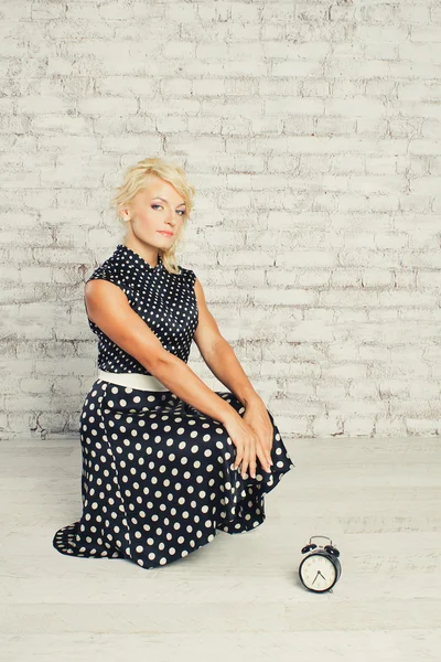Jeune fille blonde en robe assise avec horloge en studio — Photo