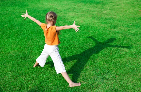 Una chica parada en la hierba mirando su sombra — Foto de Stock