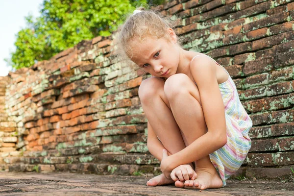 Triest klein meisje op de achtergrond van een oude bakstenen muur — Stockfoto