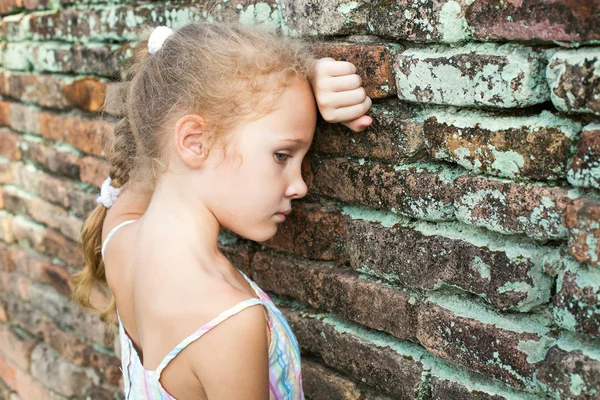 Szomorú kislány a háttérben egy régi téglafal — Stock Fotó
