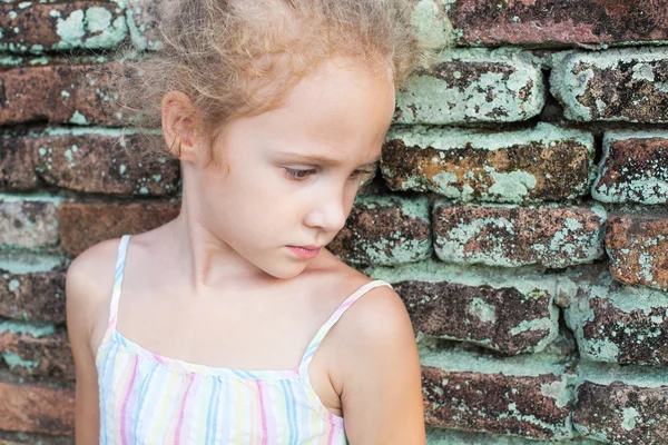 Triste menina no fundo de uma parede de tijolo velho — Fotografia de Stock