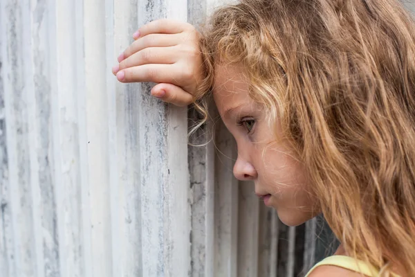 Triste menina no fundo de uma parede velha — Fotografia de Stock