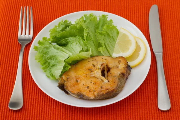 Рыба с салатом и лимоном на белой тарелке — стоковое фото