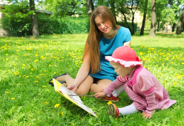 Menina e mãe lendo o livro no parque da primavera — Fotografia de Stock