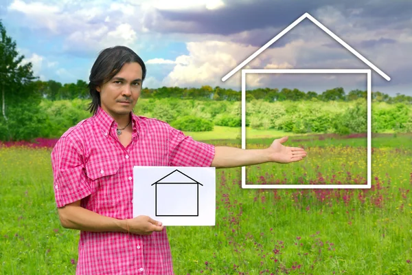 Ung man med en vit bräda med hus på en grön äng — Stockfoto