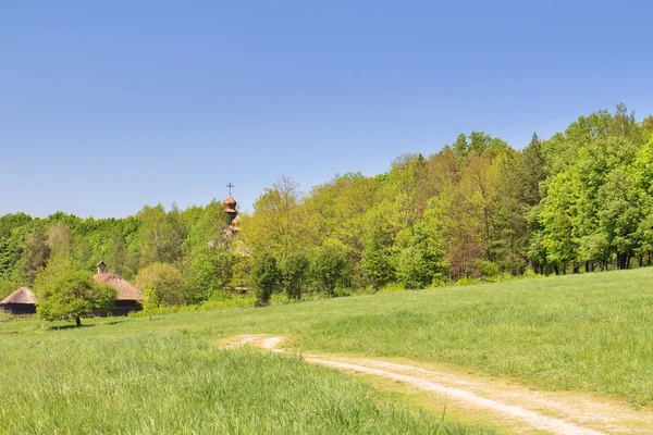 Зеленое поле, голубое небо и старая деревянная часовня — стоковое фото