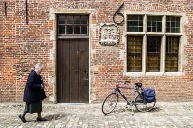 LEUVEN, BELGIUM - JUNE 13th, 2012: Old lady passes wooden door clipart