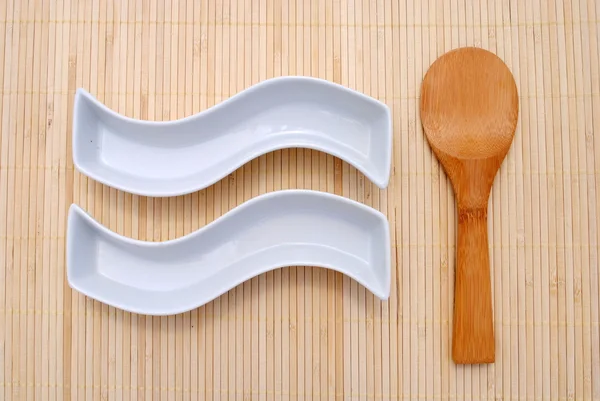 Dos platos blancos y una cuchara de madera sobre un mantel de bambú — Foto de Stock