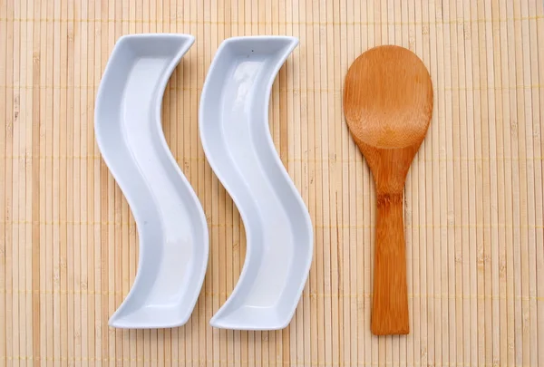 Δύο λευκά πιάτα και ένα ξύλινο κουτάλι πάνω από μια placemat μπαμπού — Φωτογραφία Αρχείου