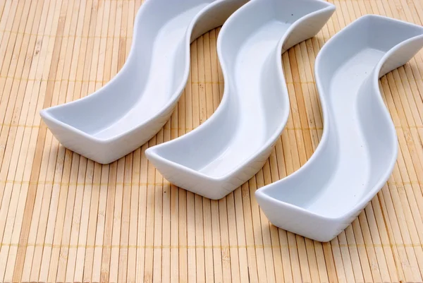 Tres platos blancos sobre un mantel de bambú — Foto de Stock