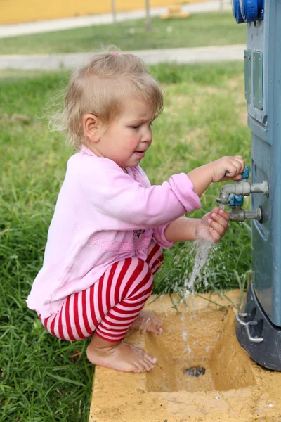 Barn flicka som leker med en vattenkran — Stockfoto